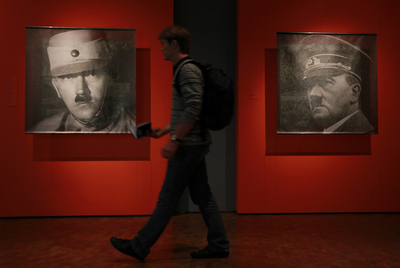 Un joven camina frente a dos retratos de Hitler expuestos en:  Hitler, la nación alemana y el crimen,  exposición inaugurada en Berlín el 15 de octubre de 2010. Abajo, uniformes del Führer.
