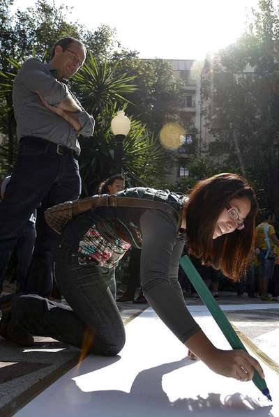 Una participante escribe en el poema gigante en honor a Miguel Hernández, ayer, en Alicante.