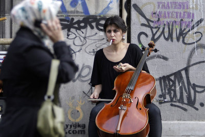 Una mujer con pañuelo islámico pasa ante una joven que toca el violonchelo en una calle de Estambul.