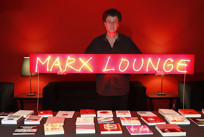 El artista chileno Alfredo Jaar, junto a la mesa con libros de la exposición   Marx Lounge.  