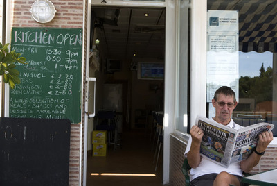 Un cliente en la terraza de un local de Orihuela que anuncia su horario y menú en inglés.