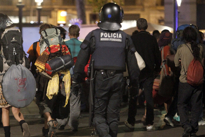 Varios acampados abandonan la plaza de Catalunya bajo la mirada de un  mosso. 
