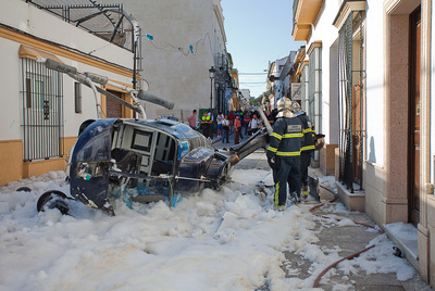 Varios bomberos examinan el helicóptero tras apagar las llamas seguidas a su caída en una calle del  Puerto de Santa María.