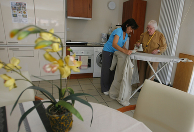 Una auxiliar del centro Lamorous ayuda a M. F. a planchar una gabardina para fortalecer sus capacidades cognitivas.