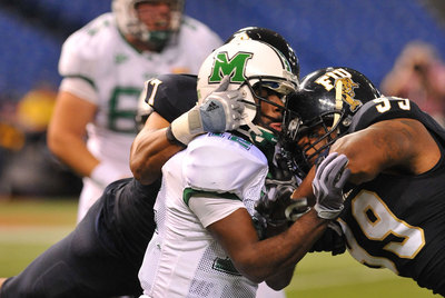 El defensa de fútbol americano Isame Faciane, con el número 99 en la camiseta negra de los International Panthers de Florida, bloquea al  quarterback  de los Marshall Thundering Herd, Rakeem Cato, en el estadio de Sant Petersburg,  Florida, en diciembre de 2011.