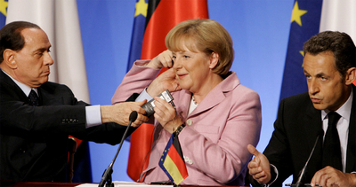 Una imagen del pasado domingo de la rueda de prensa posterior al Consejo Europeo en la que Berlusconi ayuda a la canciller a colocarse el equipo de traducción.