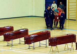 Los trabajadores de los servicios funerarios trasladan uno de los féretros.