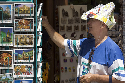Un turista contempla unas postales en el centro de Valencia con un original gorro de papel contra el sol.