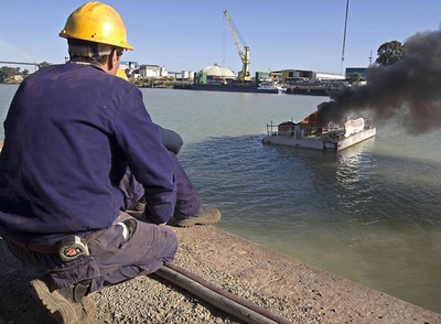 Trabajadores frente a la barcaza que ha cortado el tráfico en el río con material inflamable.