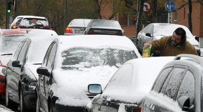 Un conductor limpia su coche de nieve en una calle de Madrid.
