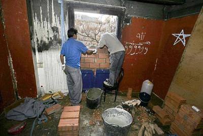 Dos obreros terminan de tapiar una de las ventanas del entresuelo de un edificio en el Raval donde ayer fue asesinado un hombre joven africano.