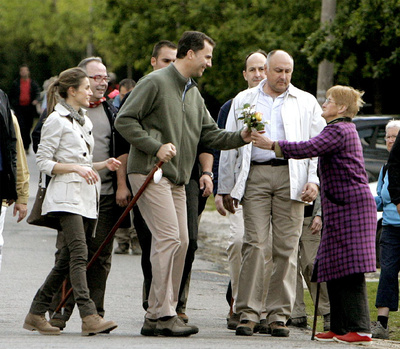 Los príncipes de Asturias reciben de manos de una vecina de Monte Gozo unas flores durante el recorrido que han realizado a pie.