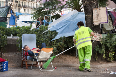 Un joven descansa en la plaza de Catalunya, mientras los servicios de limpieza trabajan a su lado, después de que los indignados hayan decidido levantar la acampada.