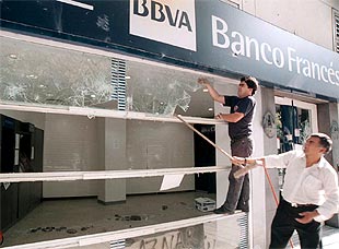 Empleados del banco reparan el establecimiento tras los destrozos provocados durante la  cacerolada  del jueves.