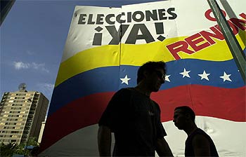 Dos opositores a Chávez caminan frente a un cartel que pide elecciones.
