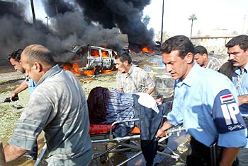 La policía iraquí evacua a un herido ante la sede de la Cruz Roja, con la ambulancia bomba aún en llamas.