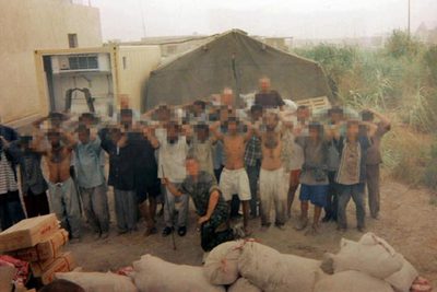 Dos soldados posan en esta fotografía con el grupo de iraquiés detenidos por robar leche en polvo. De hecho, los sacos del delito aparecen en primer término. Las Convenciones de Ginebra sobre el derecho de los prisioneros de guerra prohíben expresamente tomar imágenes de los prisioneros a modo de  souvenir. 