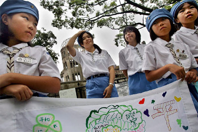 Varias colegialas llevan, como ya es habitual en la ciudad, una pancarta con mensajes de paz en el Parque Memorial de la Paz de Hiroshima. Detrás de ellas se levantan las ruinas del antiguo Salón Provincial de Exposiciones, milagroso superviviente de la bomba.
