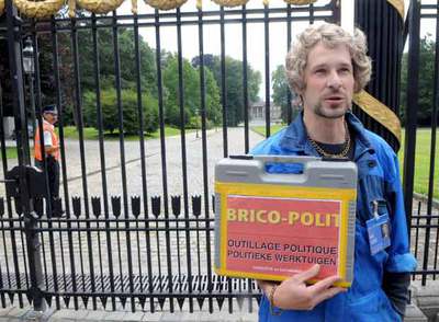 El cómico belga Nabsurde posa ante el Palacio Real disfrazado de carpintero y sosteniendo una caja en la que puede leerse 