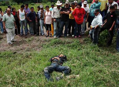 Varios vecinos contemplan el cadáver del joven que ha aparecido muerto en la localidad fronteriza con Nicaragua de El Paraíso. Según lo vecinos, el joven era partidario del retorno del presidente depuesto, Manuel Zelaya -quien ayer intentó entrar en Honduras por esa zona- por lo que fue arrestado por las fuerzas de seguridad.