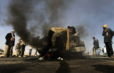 Rebeldes libios se preparan para remolcar un vehículo de las tropas de Gadafi, alcanzado por un bombardeo de la OTAN en Breba.