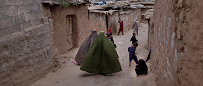 Dos mujeres caminan  al tiempo que unos niños juegan en una calle de Islamabad, Pakistán.