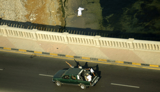 Rebeldes libios a bordo de una furgoneta pasan frente a un cadáver que flota en la orilla del mar.