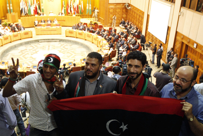 Varios ciudadanos libios sotienen una bandera de su país mientras la cumbre extraordinaria de la Liga Árabe en el Cairo ha readmitido al país en la organización.