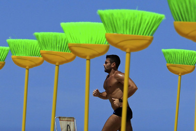 Un hombre corre entre las escobas verdes en la playa de Copacabana.