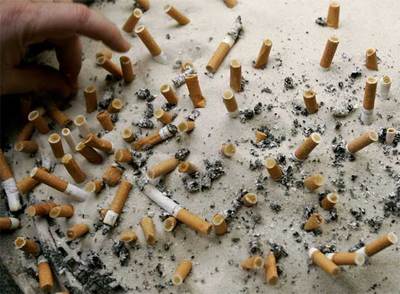 Un fumador apaga una colilla en un cenicero a las puertas de una oficina.