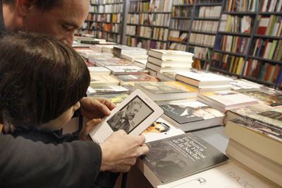 Usuarios de Kindle,  e-book  de Amazon, leen un libro electrónico en una librería de Madrid.